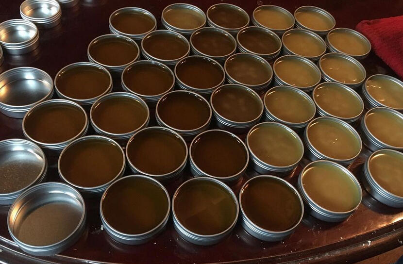 Open tins of salves freshly poured. Some have cooled and turned a lighter color, some are still hot and dark colored