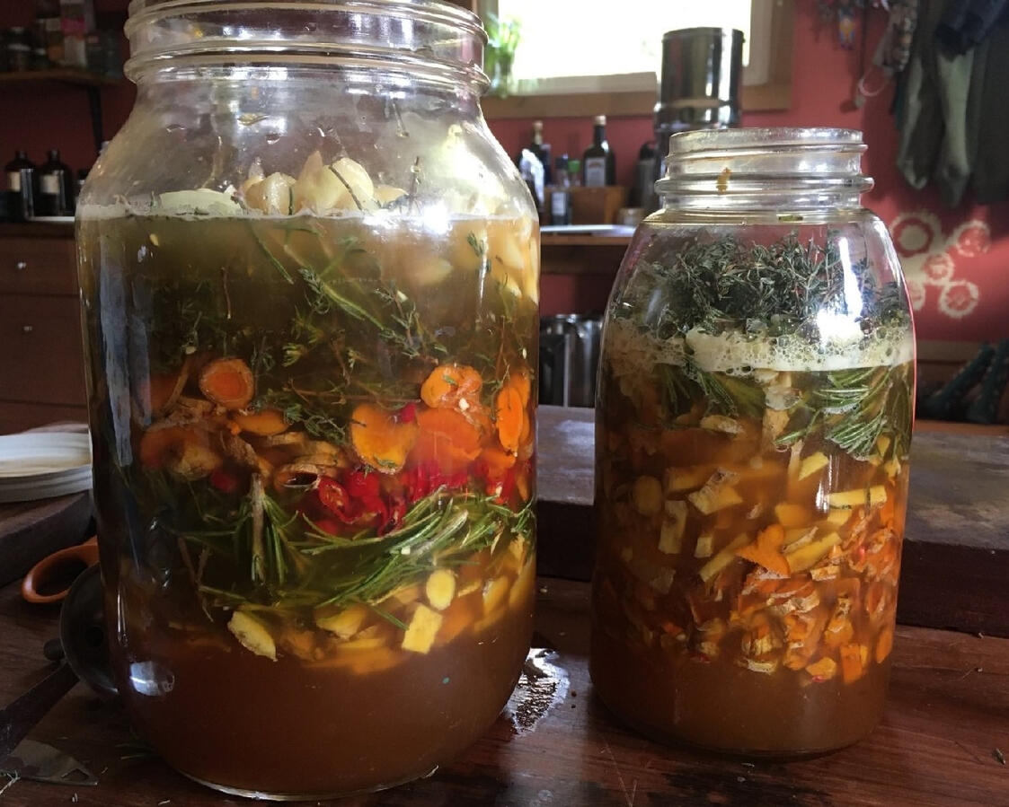 jars of freshly assembled fire cider, ingredients including herbs, like rosemary and thyme, and roots, like horseradish, covered in vinegar